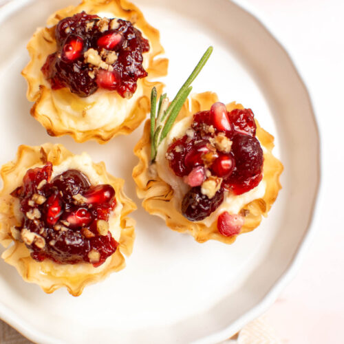 Three cranberry brie bites with pomegranate and pecans on small round dish.