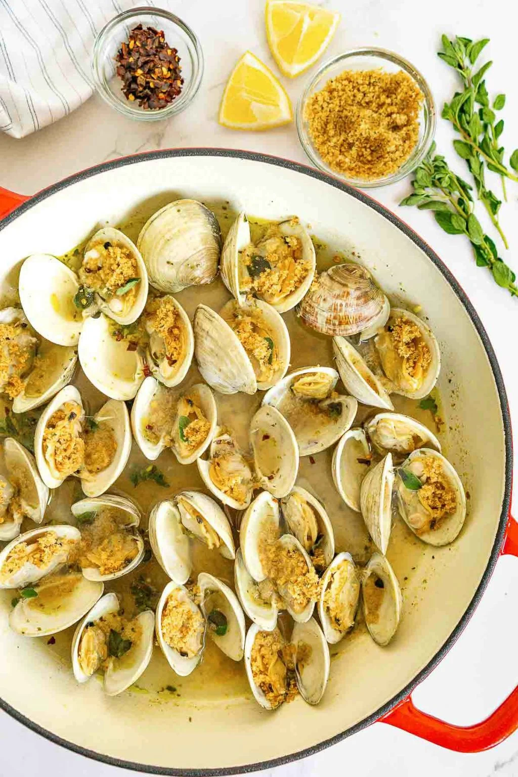 Clams oreganata in a large skillet with breadcrumbs and green garnish.