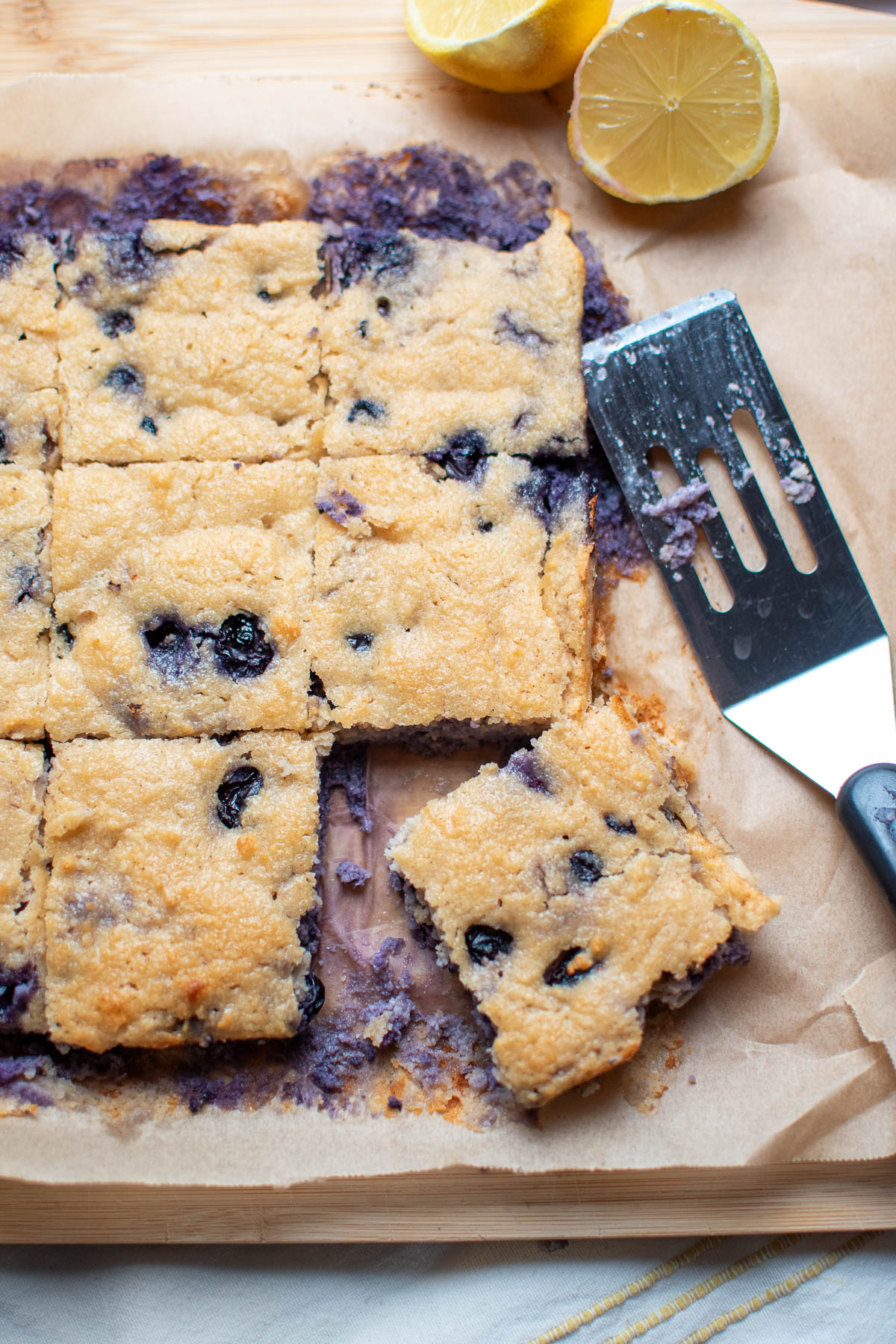 Piece of blueberry breakfast bake pulled away from the rest of the squares on brown parchment paper.