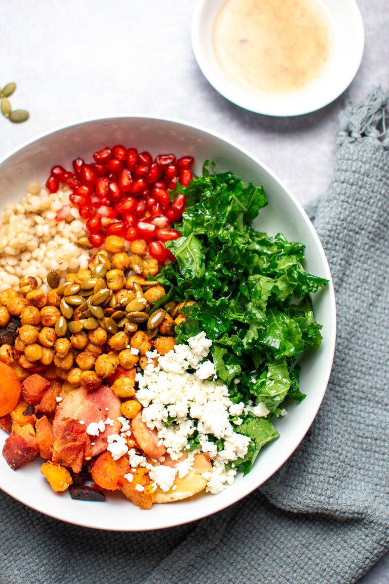 White bowl with different ingredients arranged in groups including chickpeas, roasted vegetables, and kale.