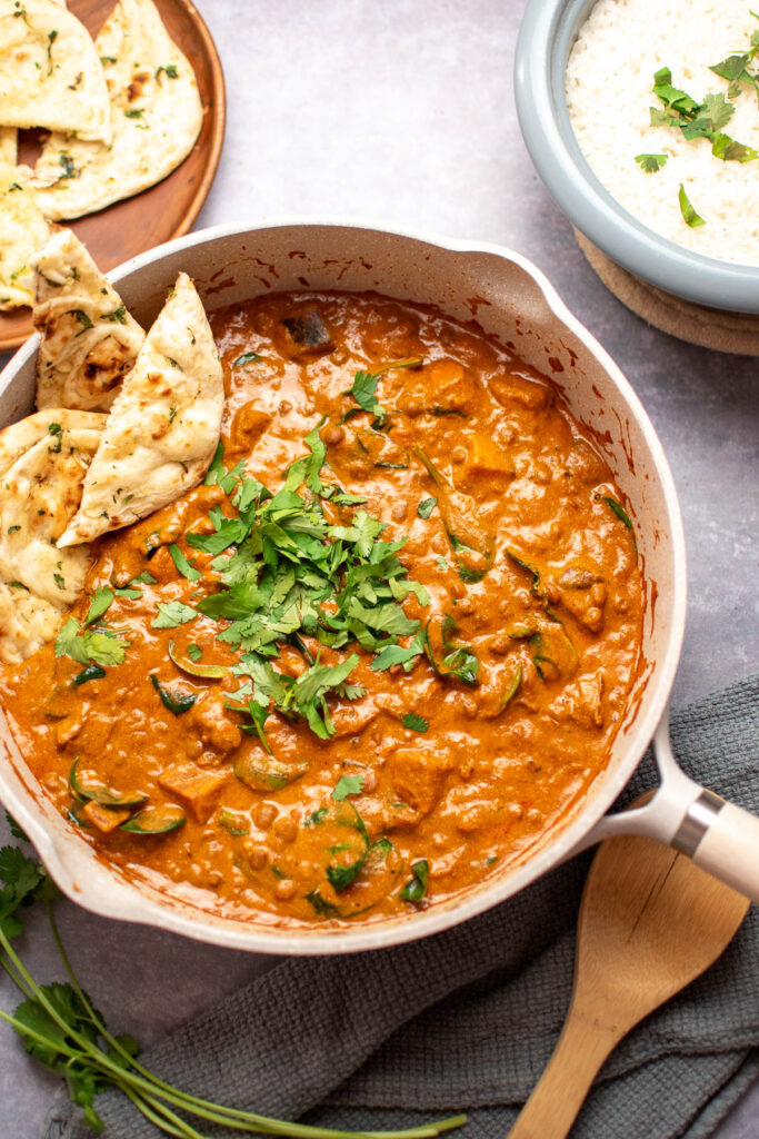 Lentil curry in a large white Dutch oven with green garnish and flat bread.