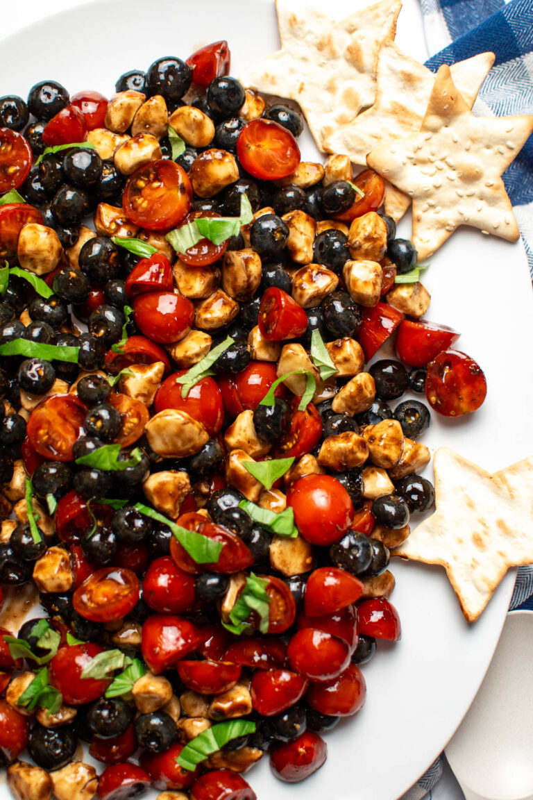 Caprese salad with tomatoes, blueberries, and mozzarella on white plate with star crackers.