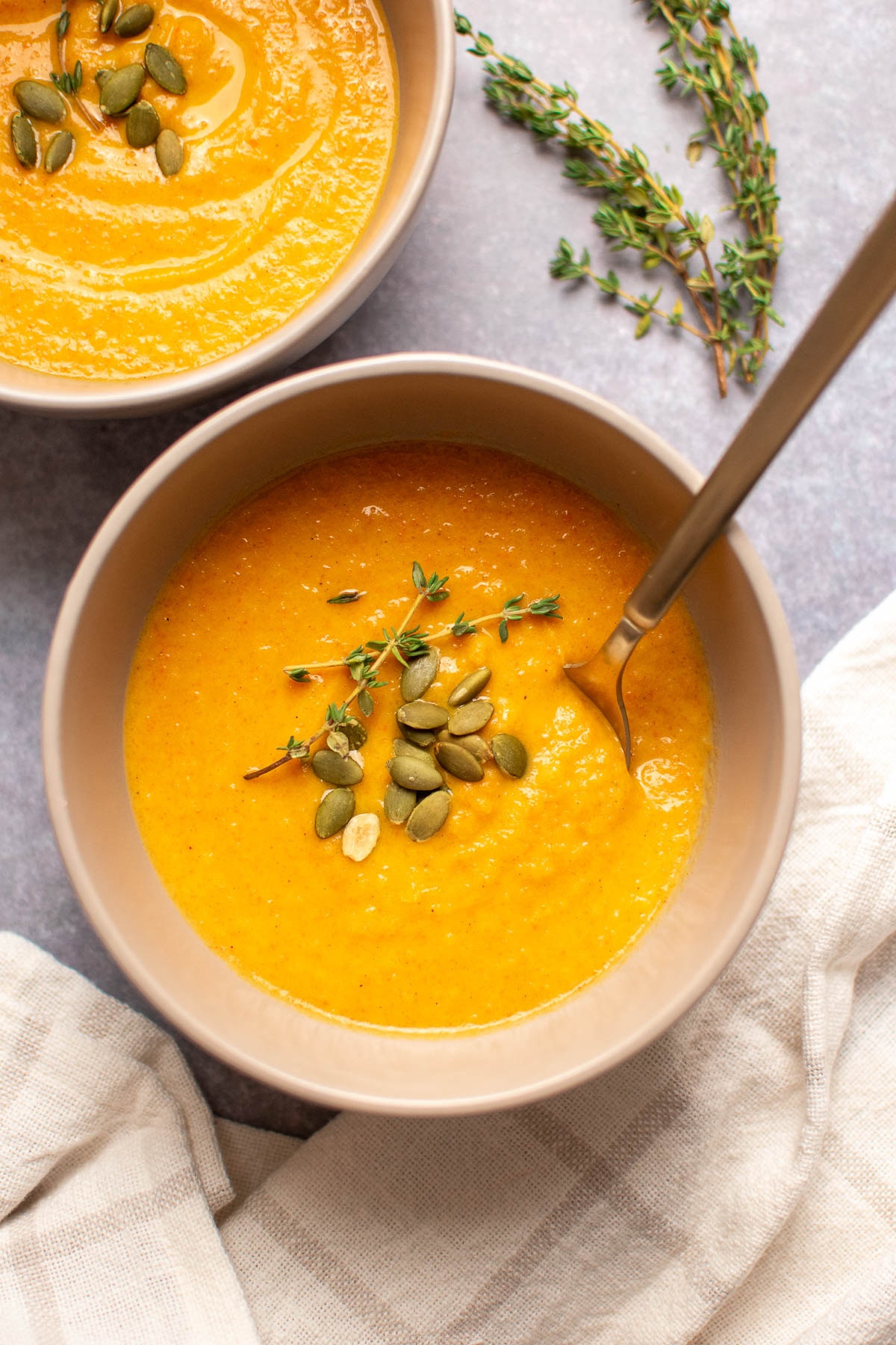 Bowl of apple cider harvest soup with pumpkin seeds on table with patterned towel nearby.