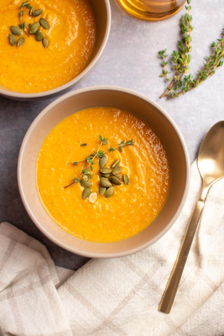 Beige bowl full of apple cider harvest soup with gold spoon and towel nearby.