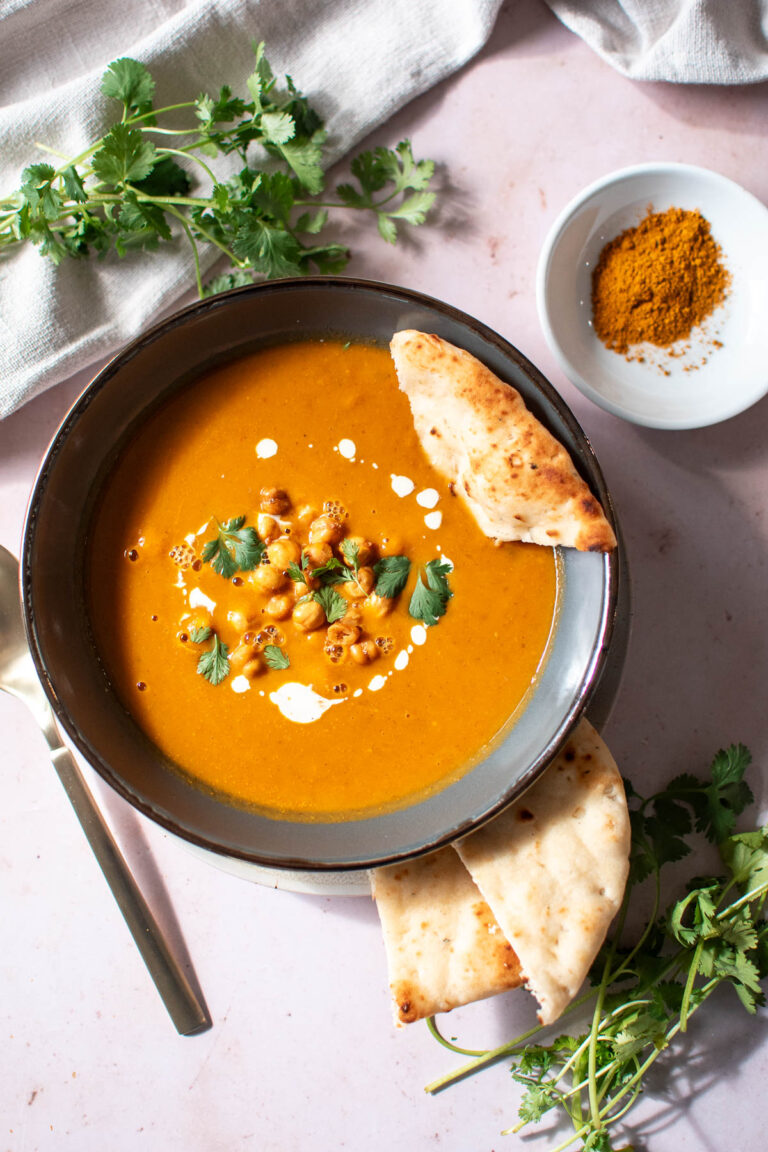 Naan bread rests in bowl of curried pumpkin coconut soup with fresh cilantro nearby.