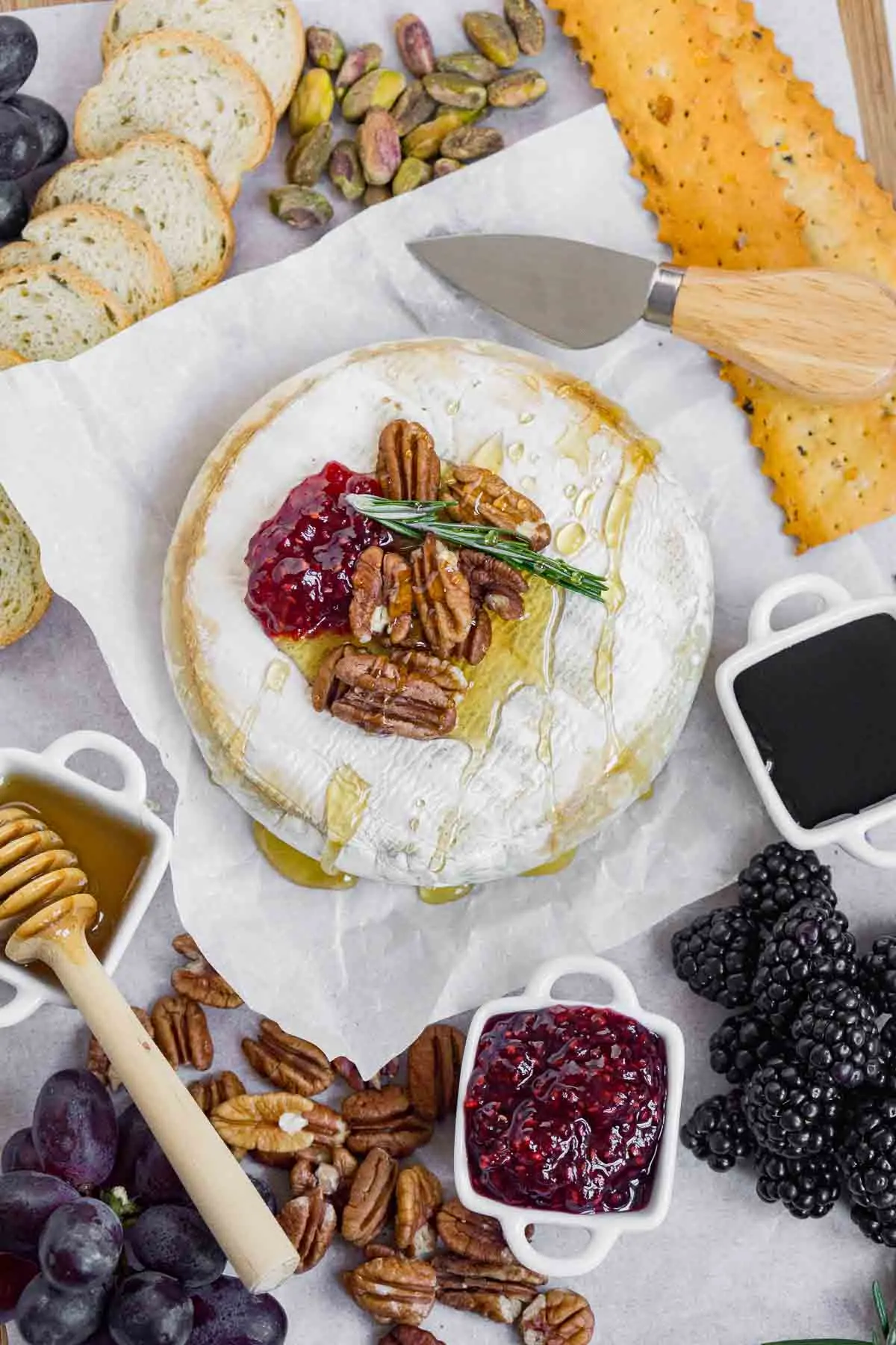 Air fryer brie with pecans and jam on parchment paper with bread and crackers.