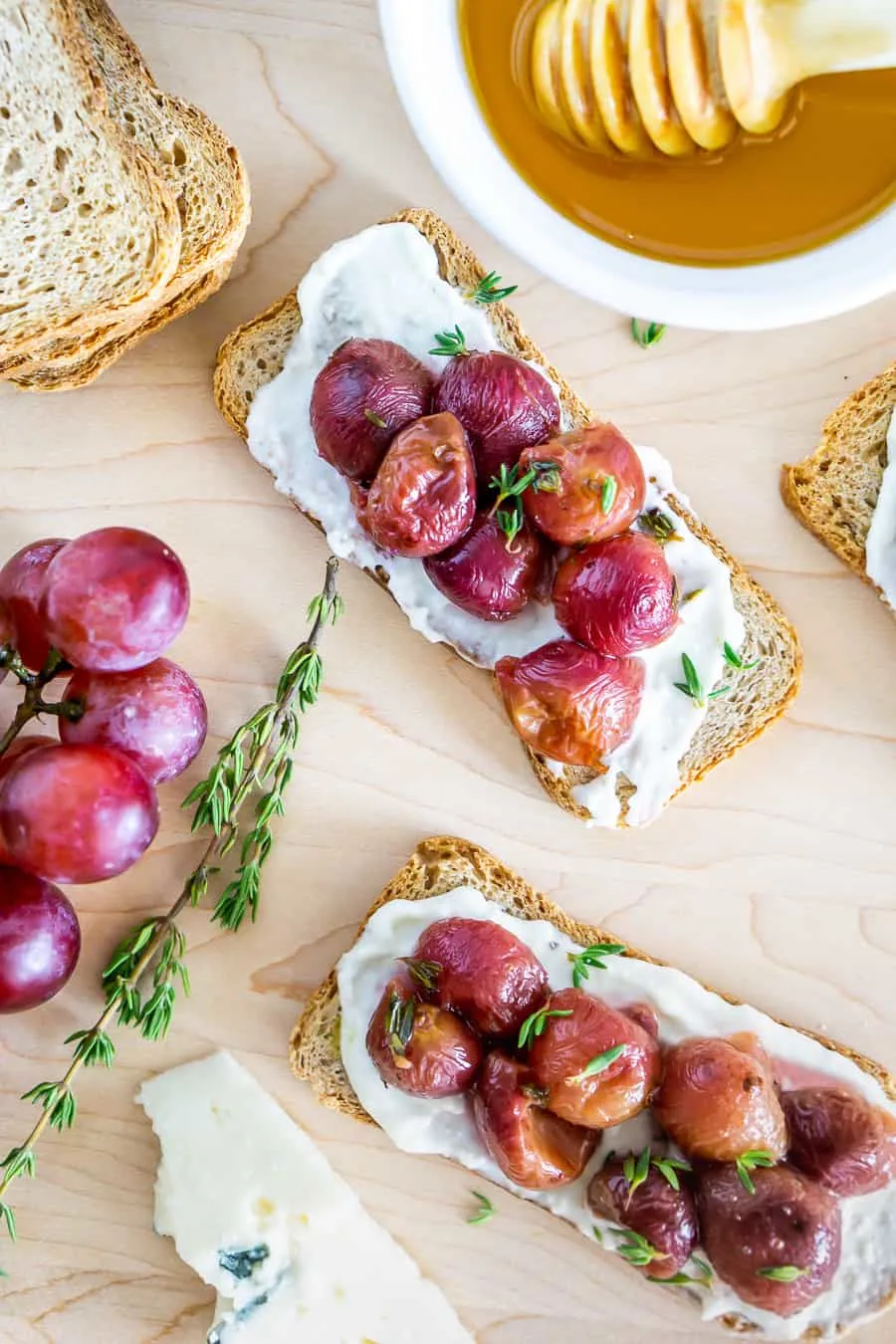 Crostini with creamy white cheese and blistered grapes with green garnish.