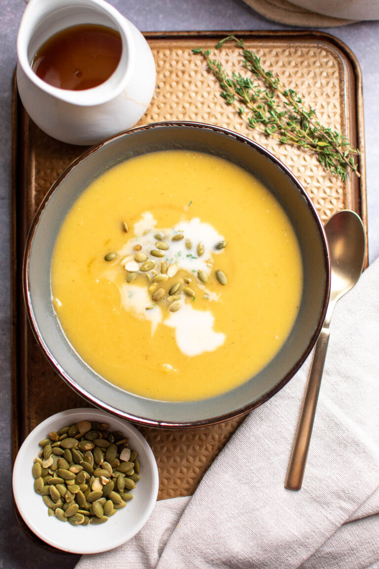 Gray bowl of acorn squash soup on metal baking sheet with different ingredients nearby.