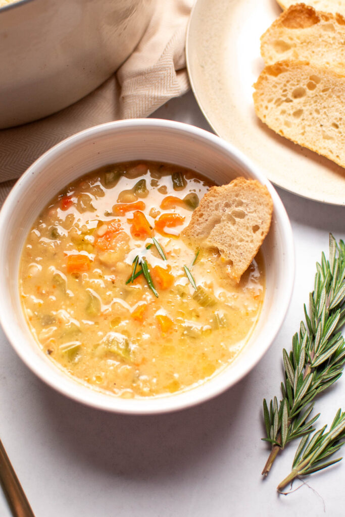 Bowl of white bean soup with piece of crusty bread in broth.