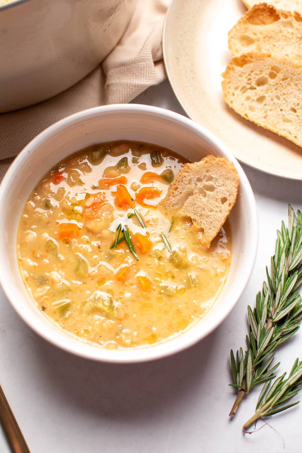 Bowl of white bean soup with piece of crusty bread in broth.