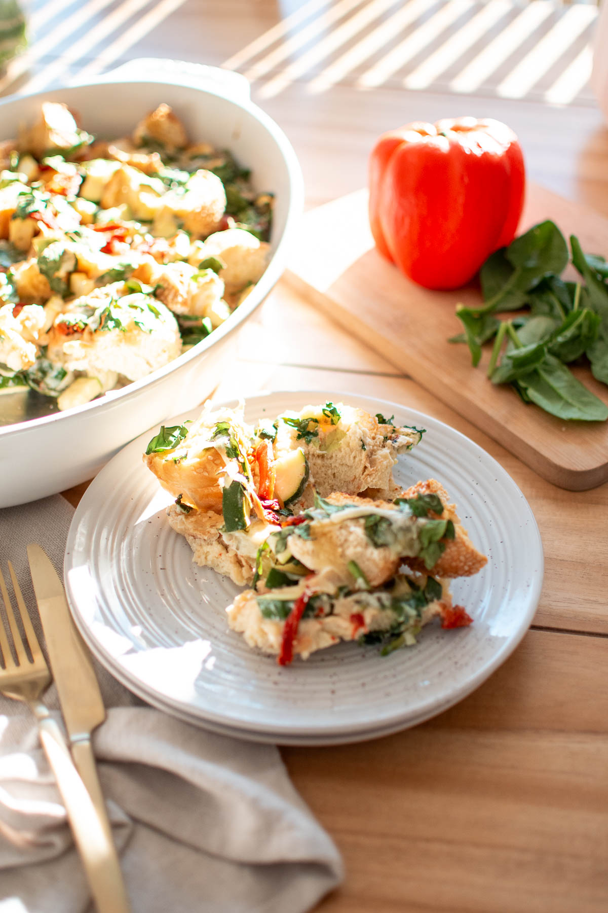 Pieces of veggie and egg strata on cream plate with gold utensils nearby.