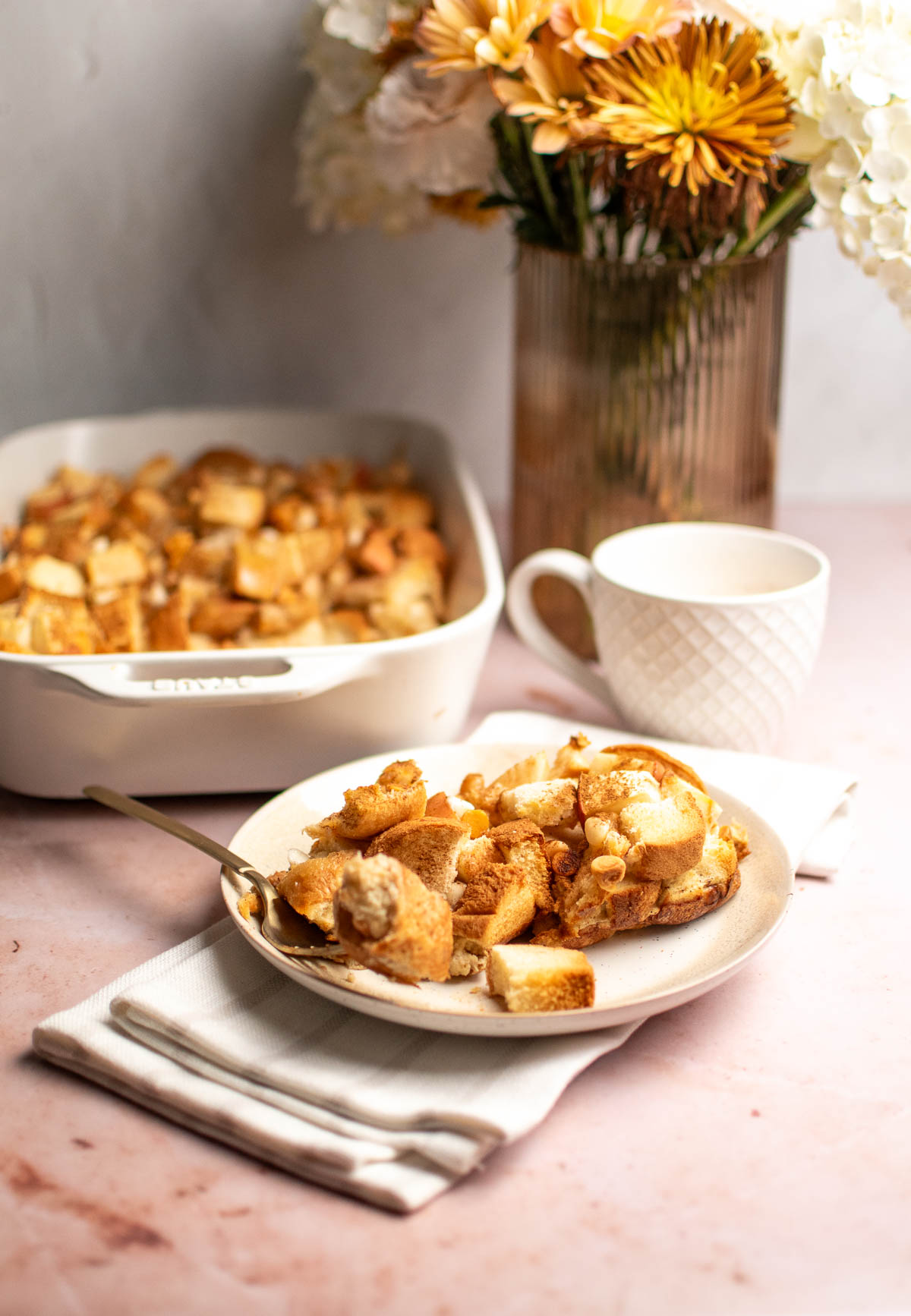 Plate of eggnog bread pudding next to baking dish of casserole and mug of eggnog.