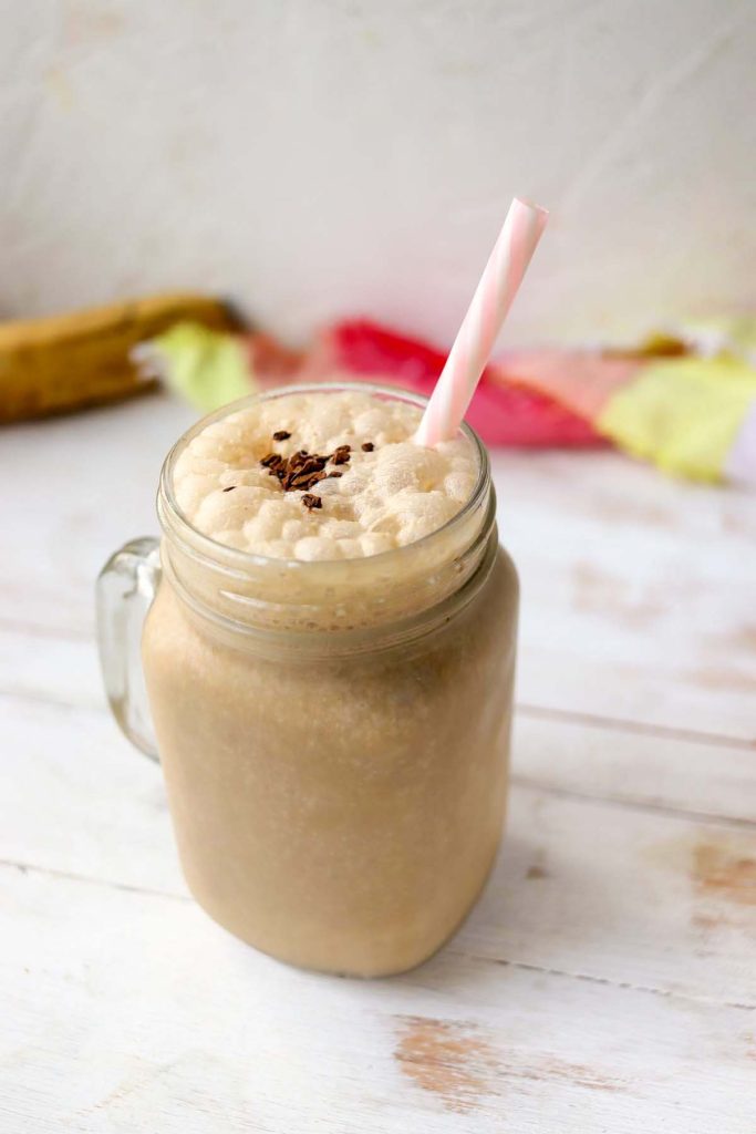 A protein smoothie in a mason glass mug with a plastic straw.