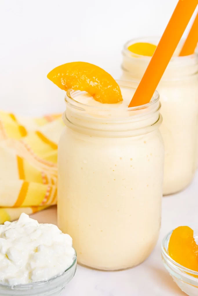 A cottage cheese smoothie with Peach slices and an orange straw.
