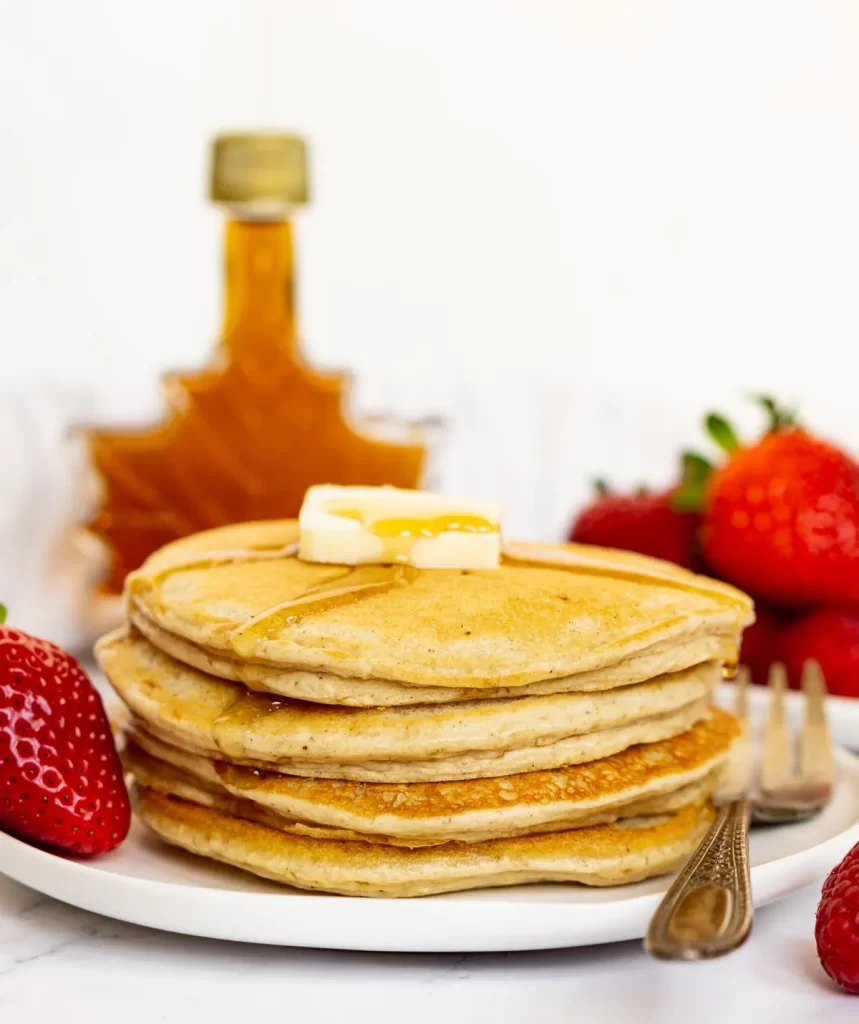 high protein pancakes on a white plate with butter, syrup, and strawberries.