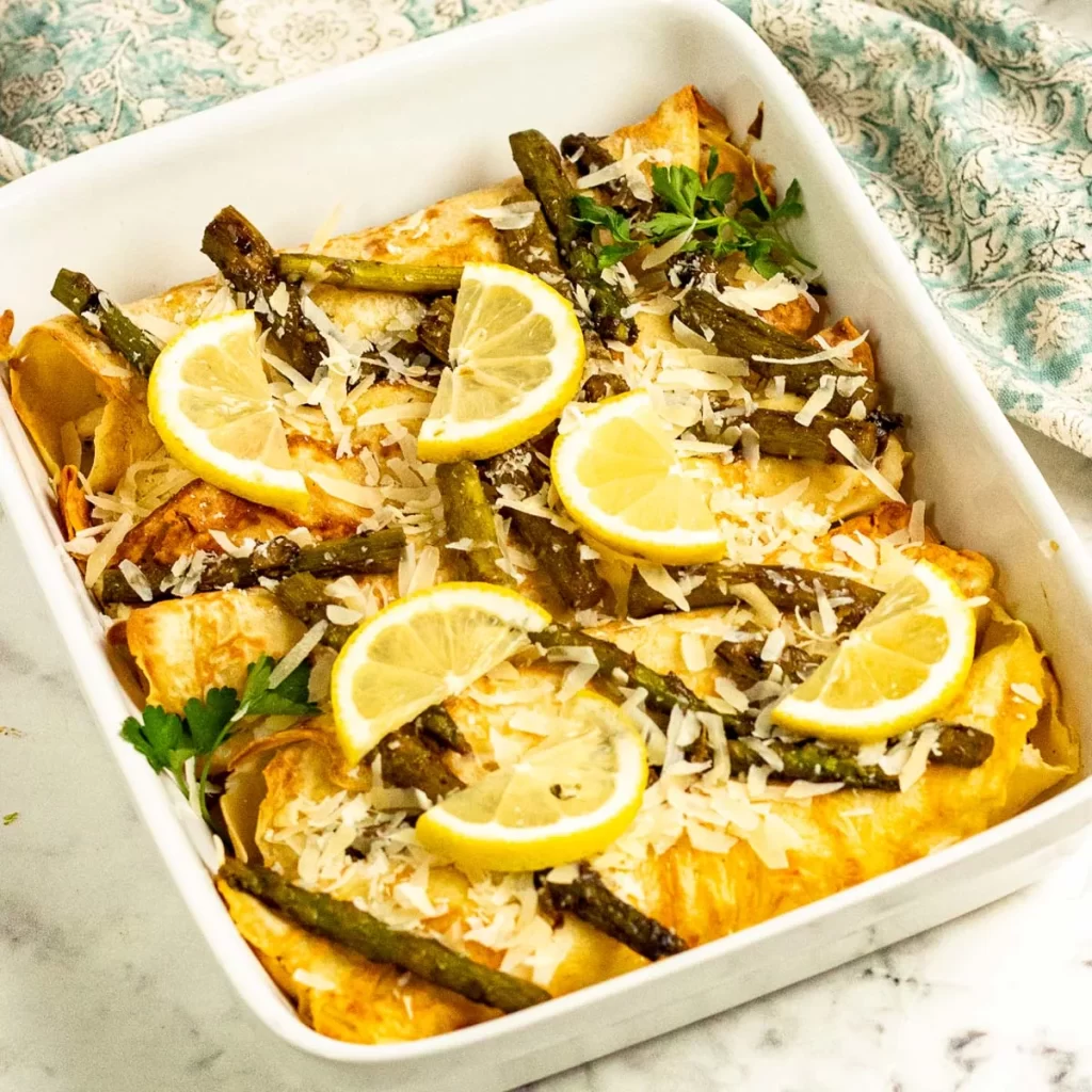 Savory chicken crepes in a white casserole baking dish with lemon slices.