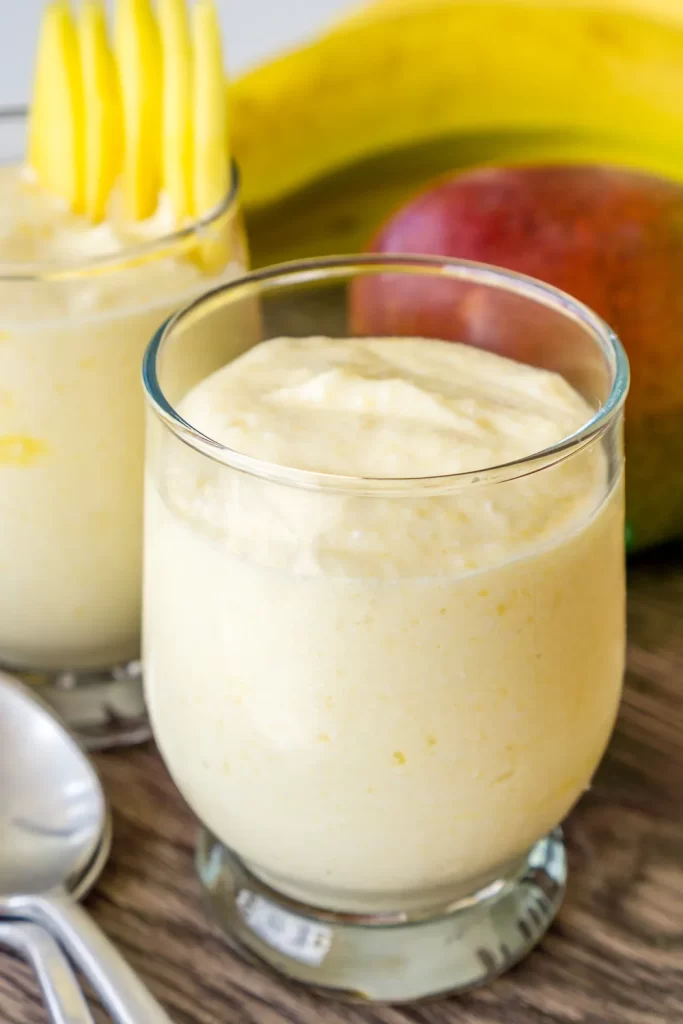A mango cottage cheese smoothie in a glass with the ingredients behind.