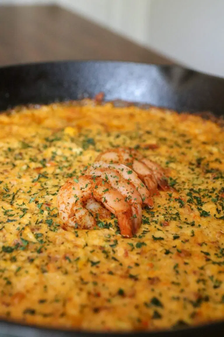 Seafood dip in a large black skillet with shrimp on top.