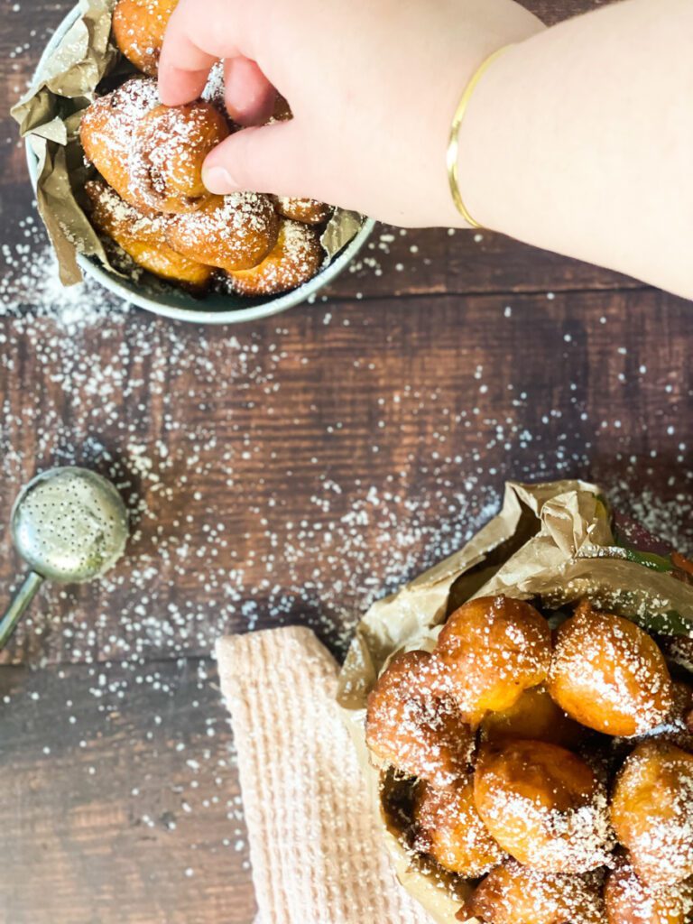Carnival fritters with powdered sugar on a wood cutting board.