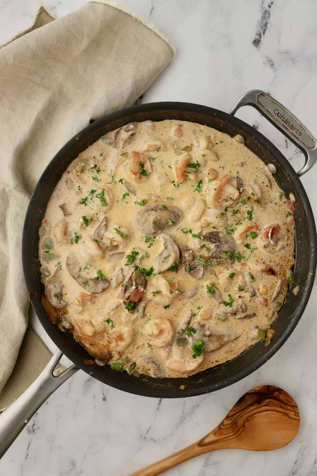 Creamy shrimp with mushrooms and green garnish in a large skillet.
