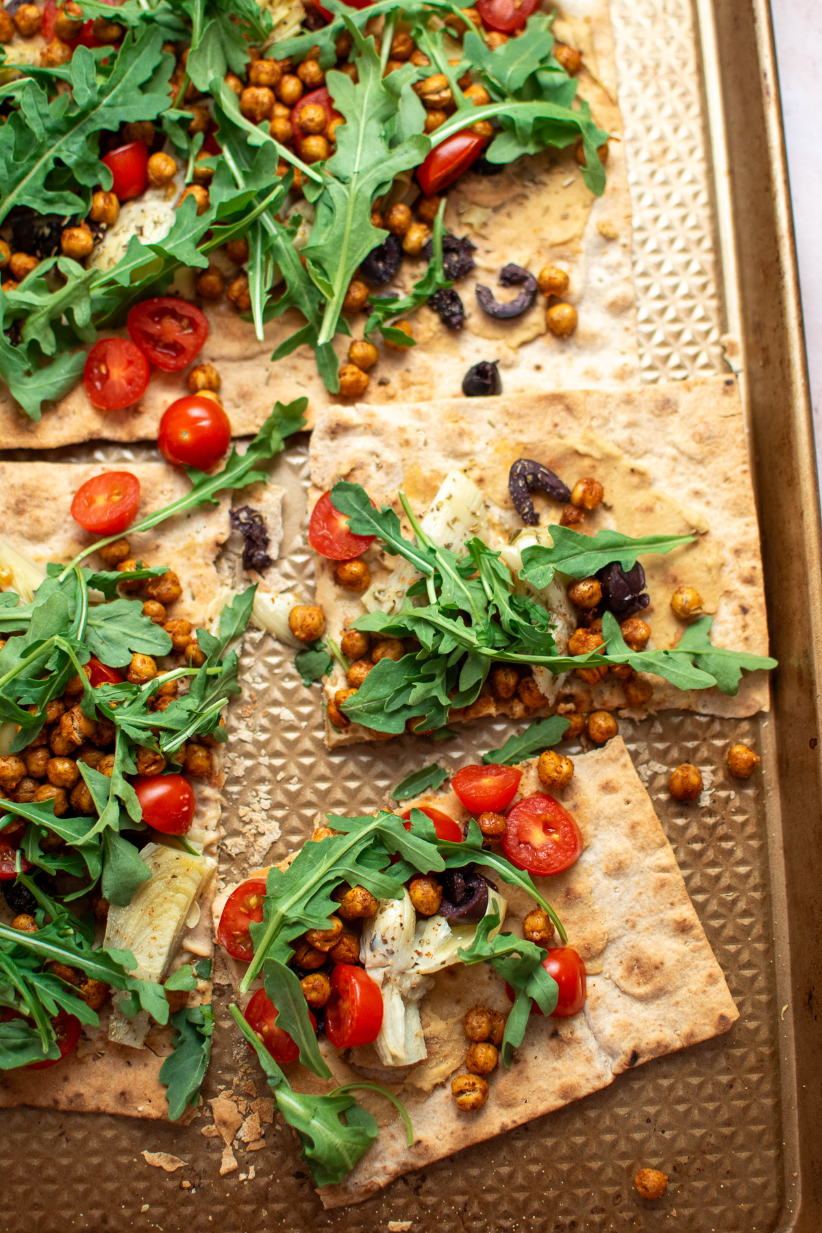 Slices of Mediterranean flatbread pizza on a sheet pan, topped with arugula.