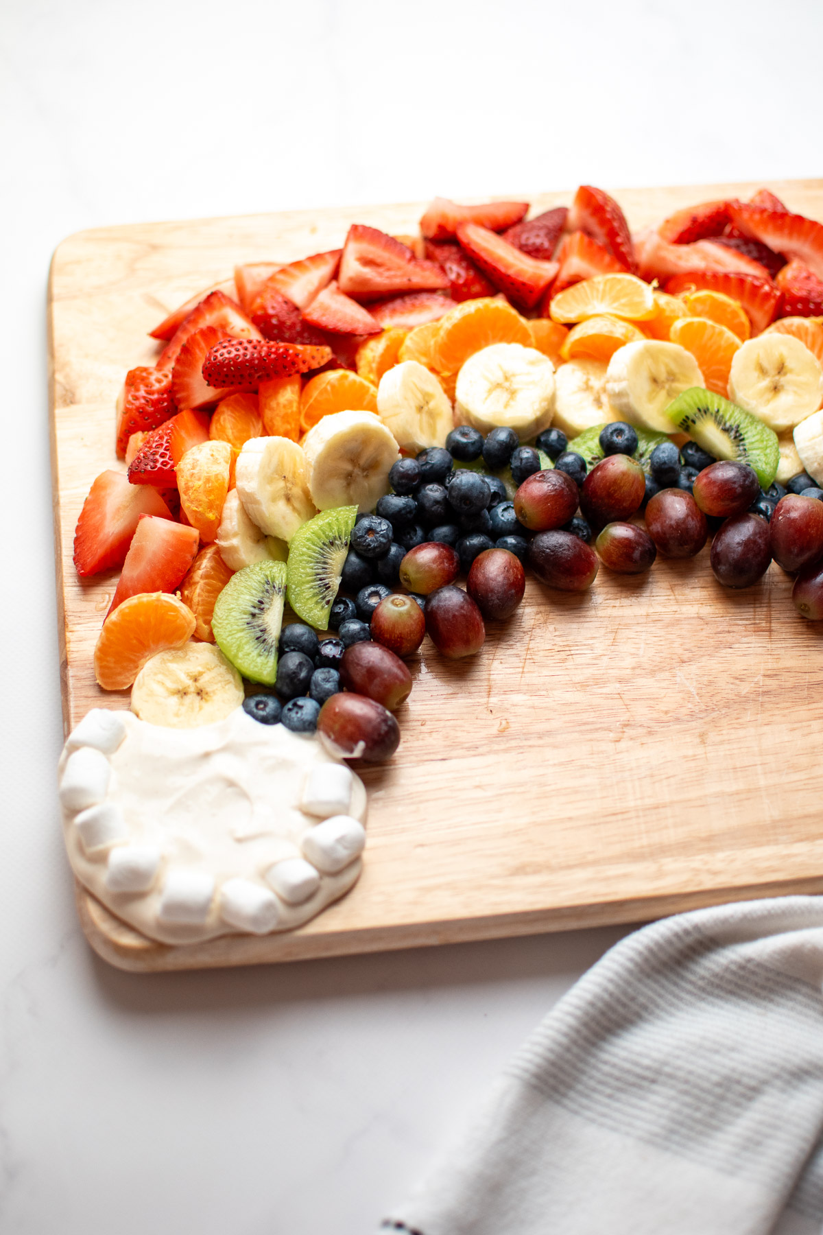 Sliced fruit arranged in a rainbow with yogurt and marshmallow clouds on a wo