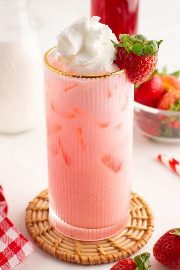 Strawberry cream soda in a gold-rimmed glass with whipped cream and fresh strawberries on top.