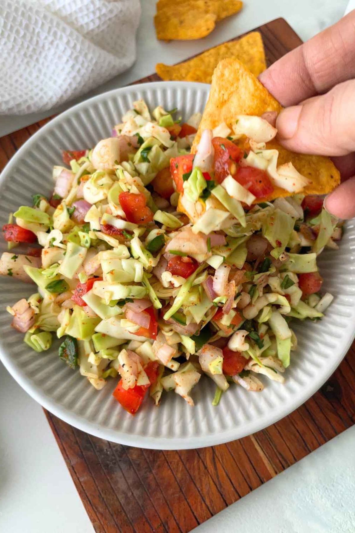Cabbage pico de gallo in a bowl and lifted from the bowl on a tortilla chip.