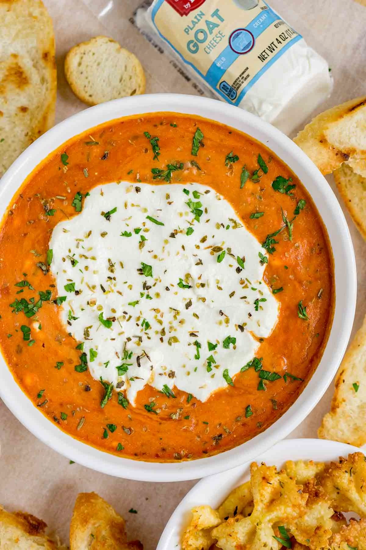 Goat cheese marinara dip in a white bowl with green garnish.