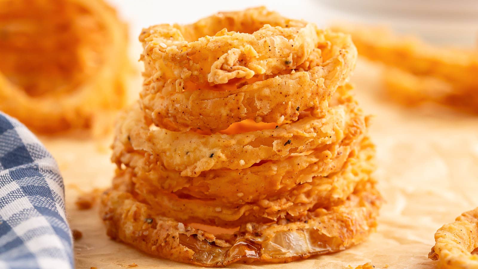A stack of homemade onion rings on a wooden cutting board.