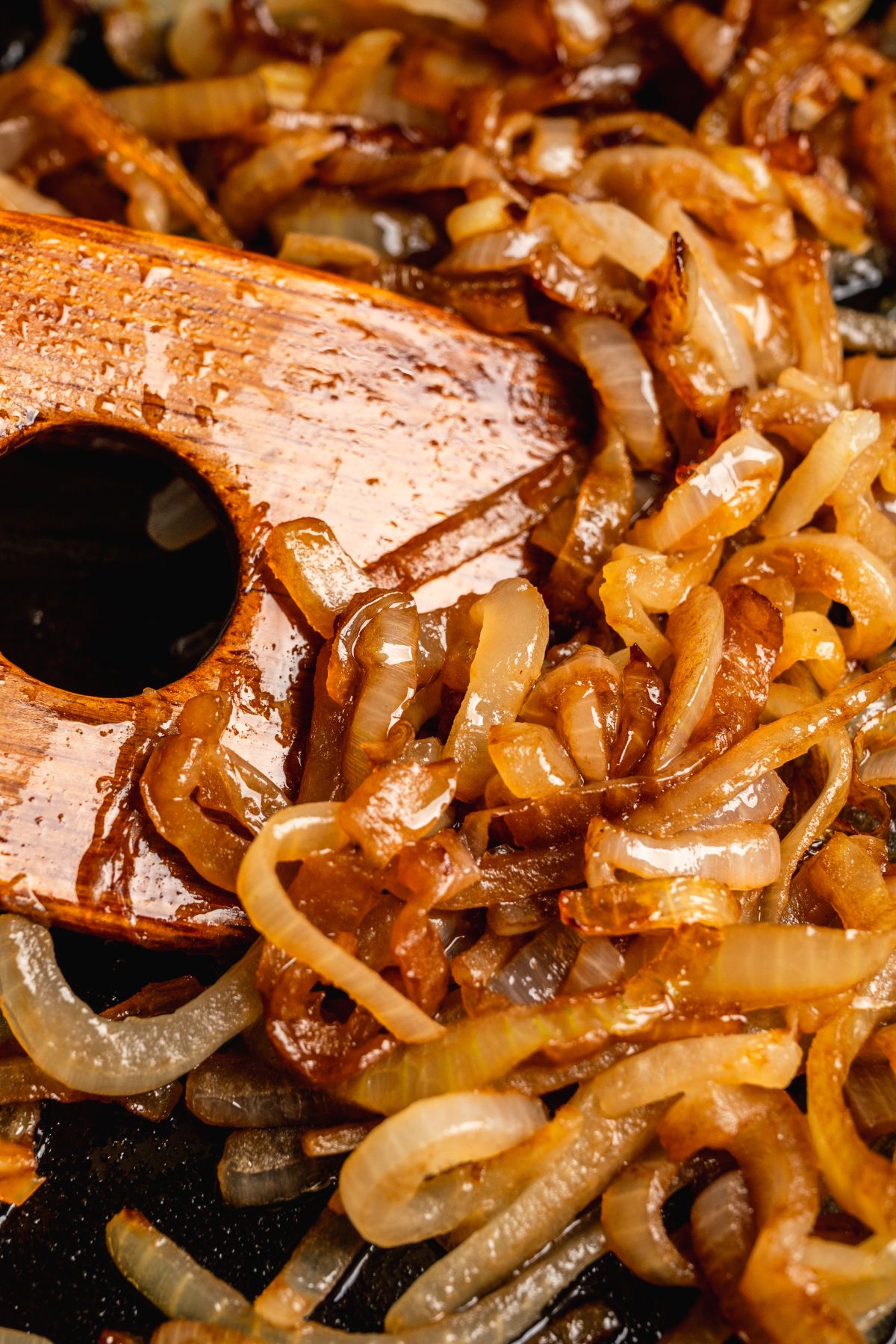 Caramelized onions in a skillet with a wooden spatula.