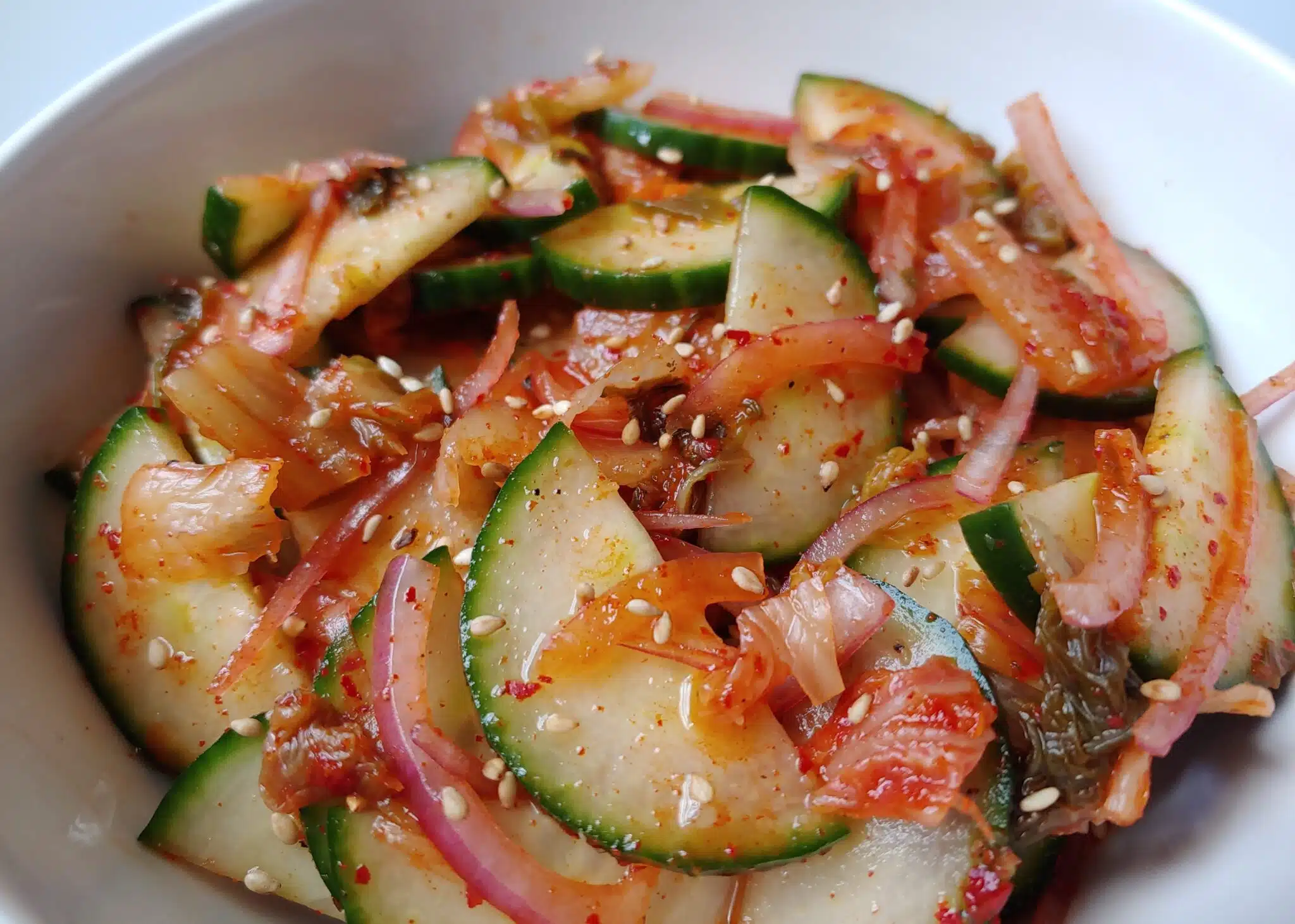 Korean kimchi cucumber salad with onion and sesame seeds in a bowl.