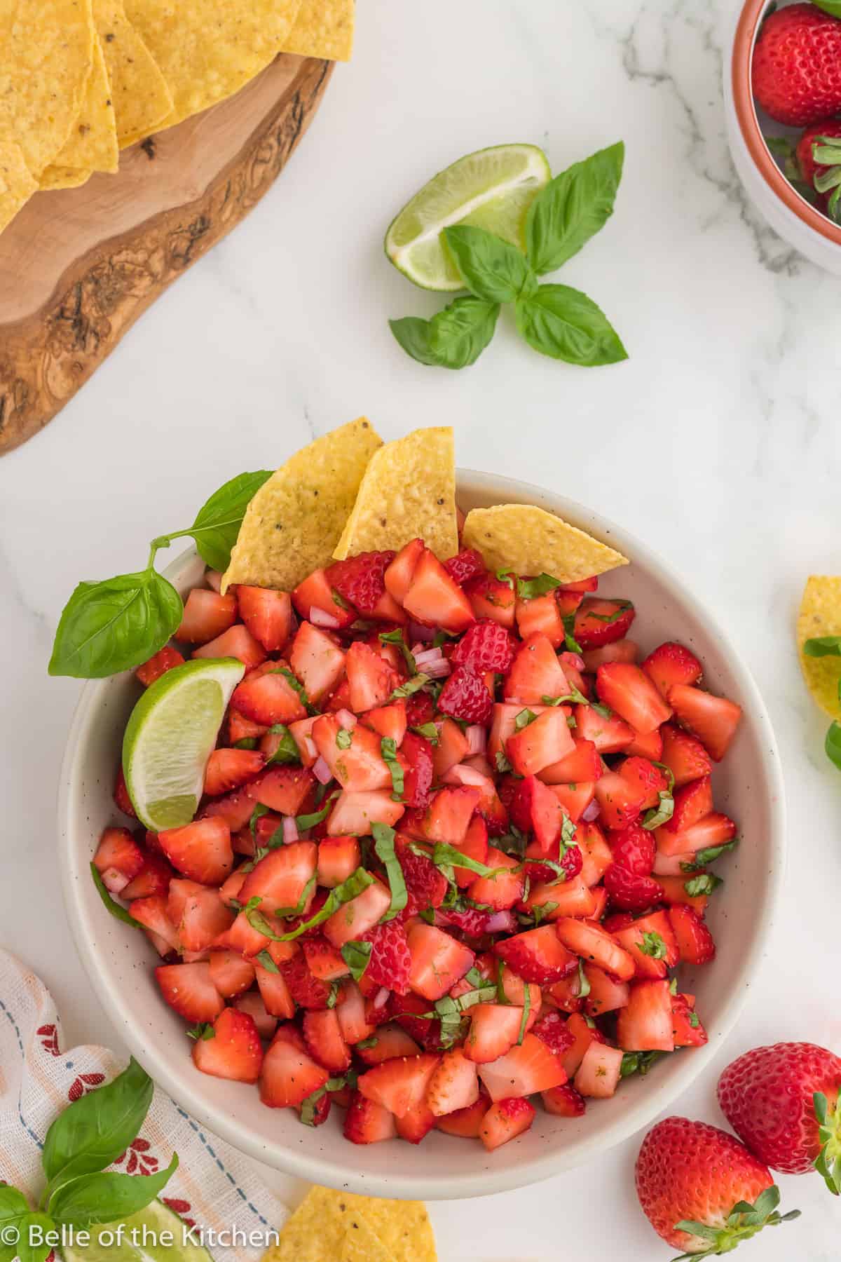 Strawberry salsa in a white bowl with a lemon wedge and tortilla chips.