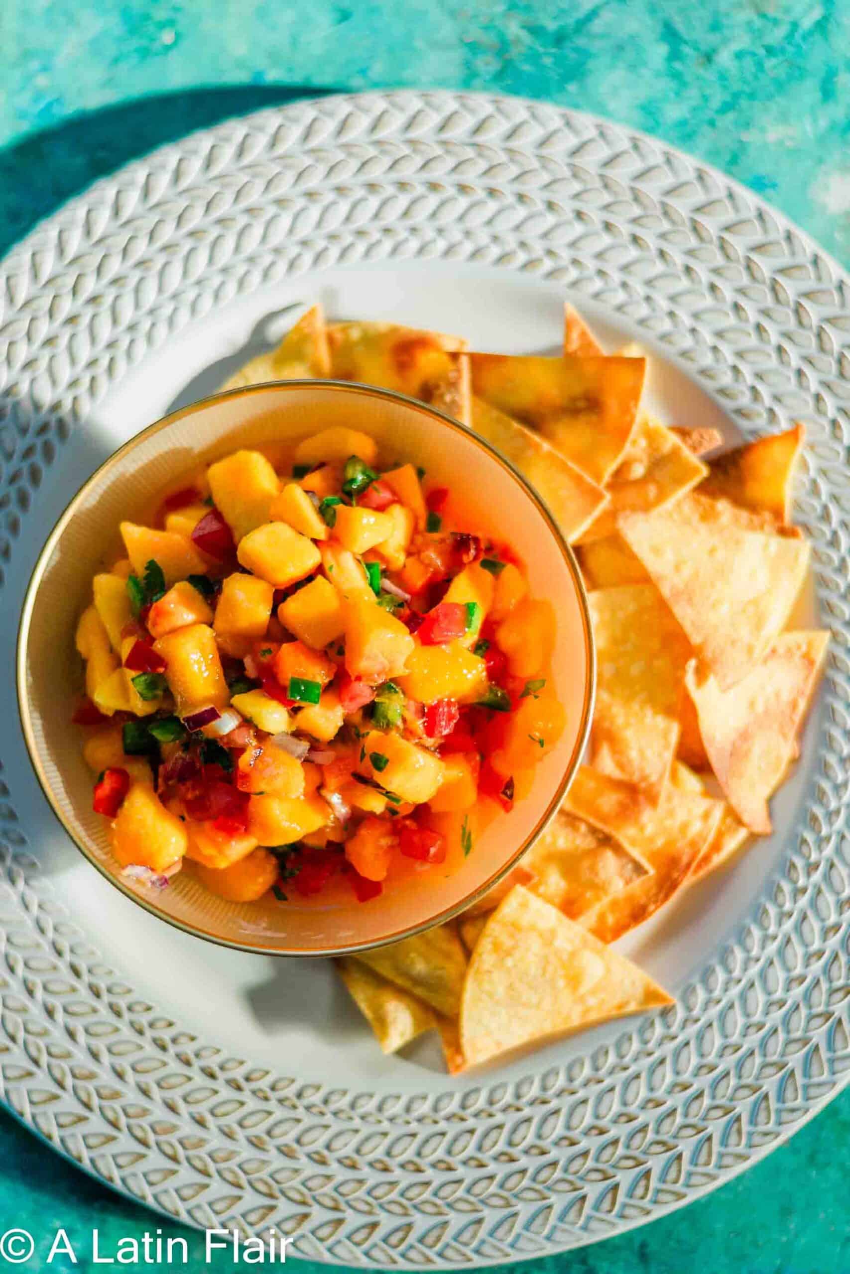 Mango salsa in a bowl that's on a plate with tortilla chips.