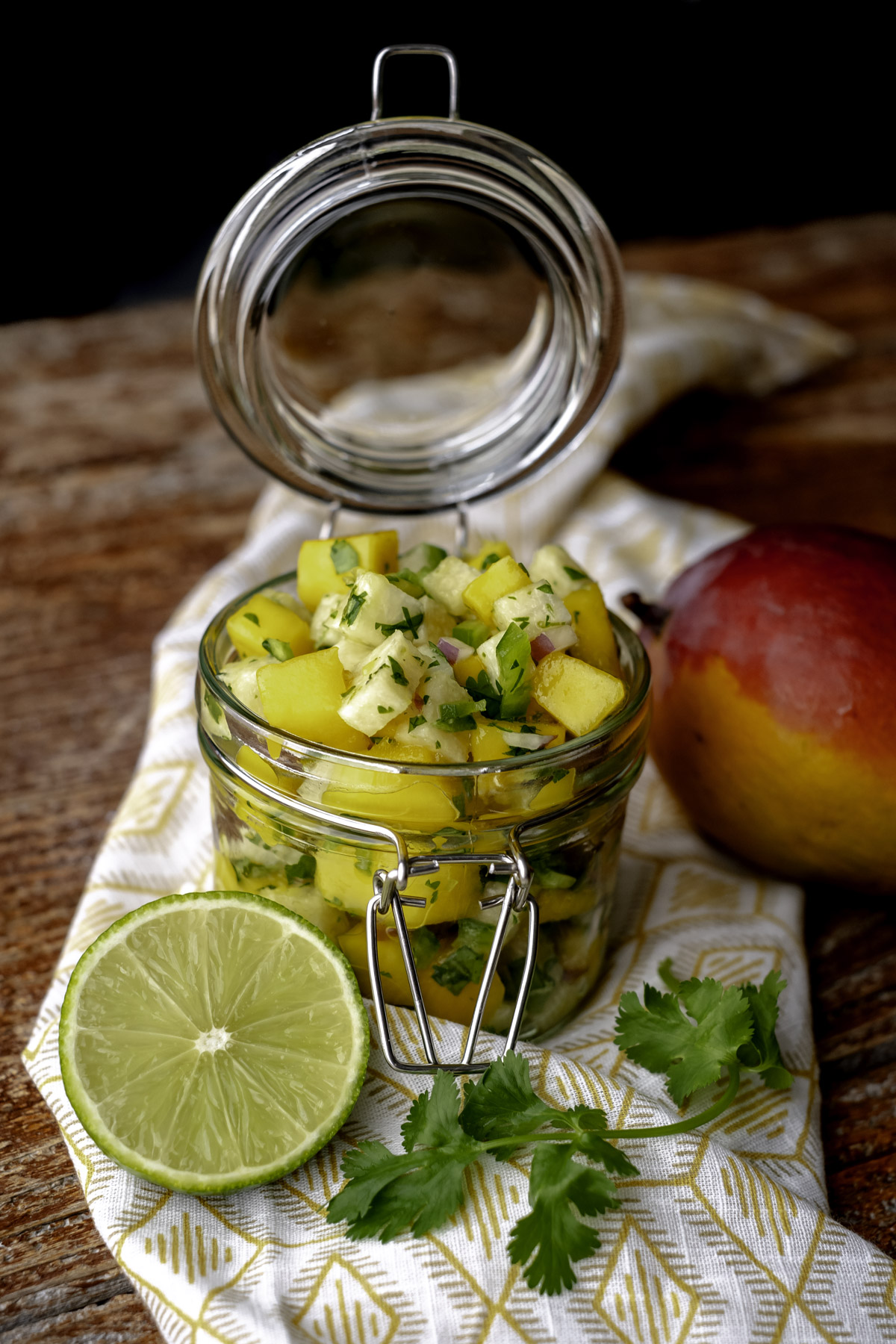 Mango jicama salsa in a mason jar next to a sliced lime and fresh mango.