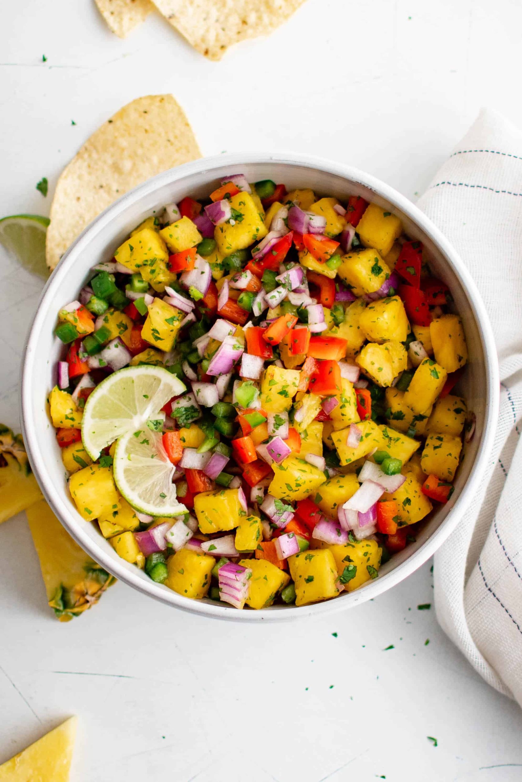 Pineapple salsa in a bowl with lime wedges and green garnish.