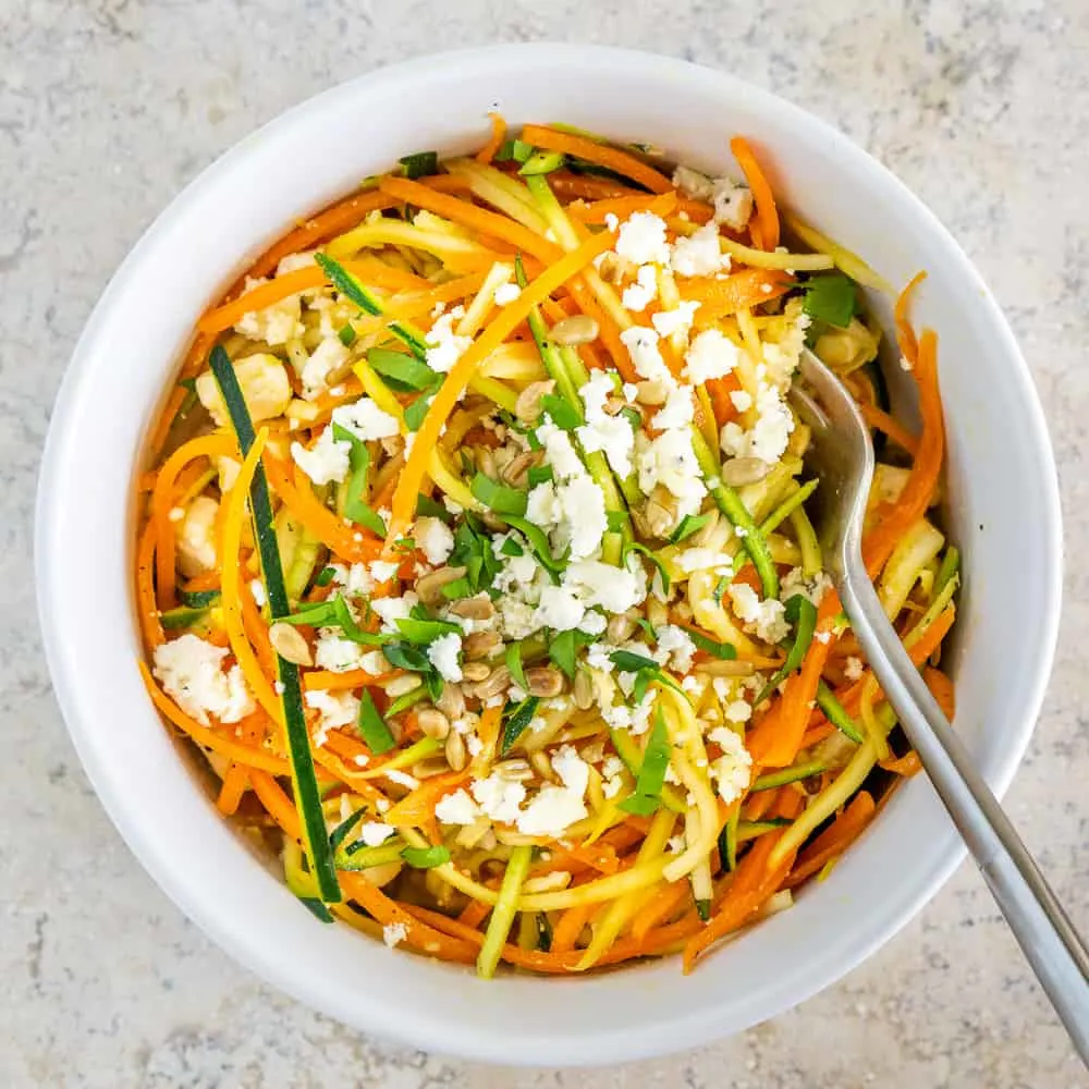 Spiralized carrot and zucchini salad with feta in a white bowl.