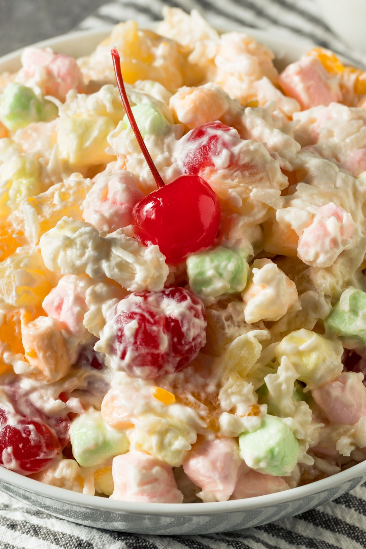 Classic ambrosia salad with colorful marshmallows and a cherry on top.