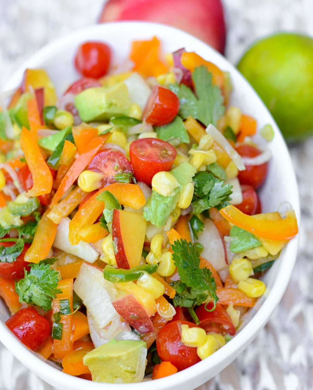 Marinated vegetable salad in a white bowl next to a lime and red vegetable.