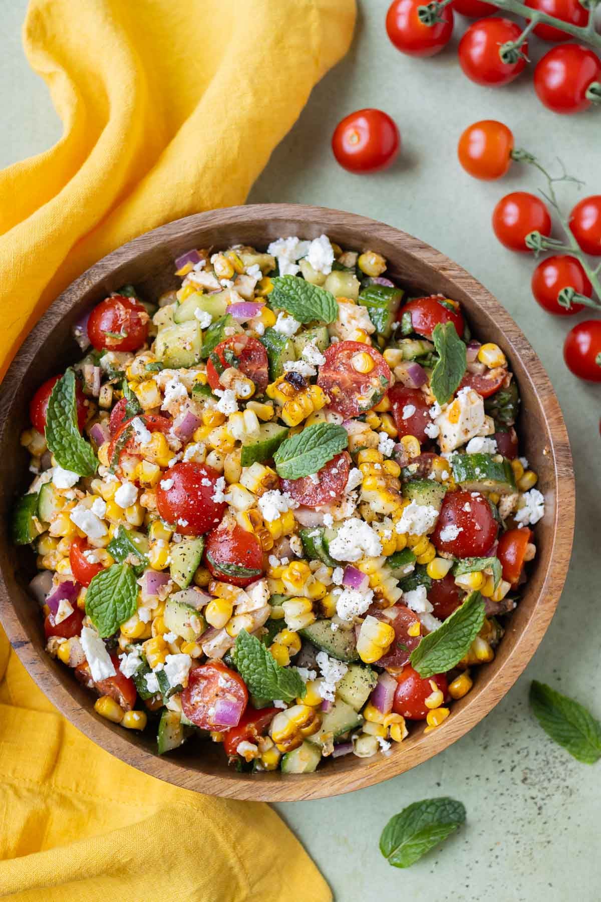 Corn and tomato salad in a wood bowl over a yellow kitchen towel.