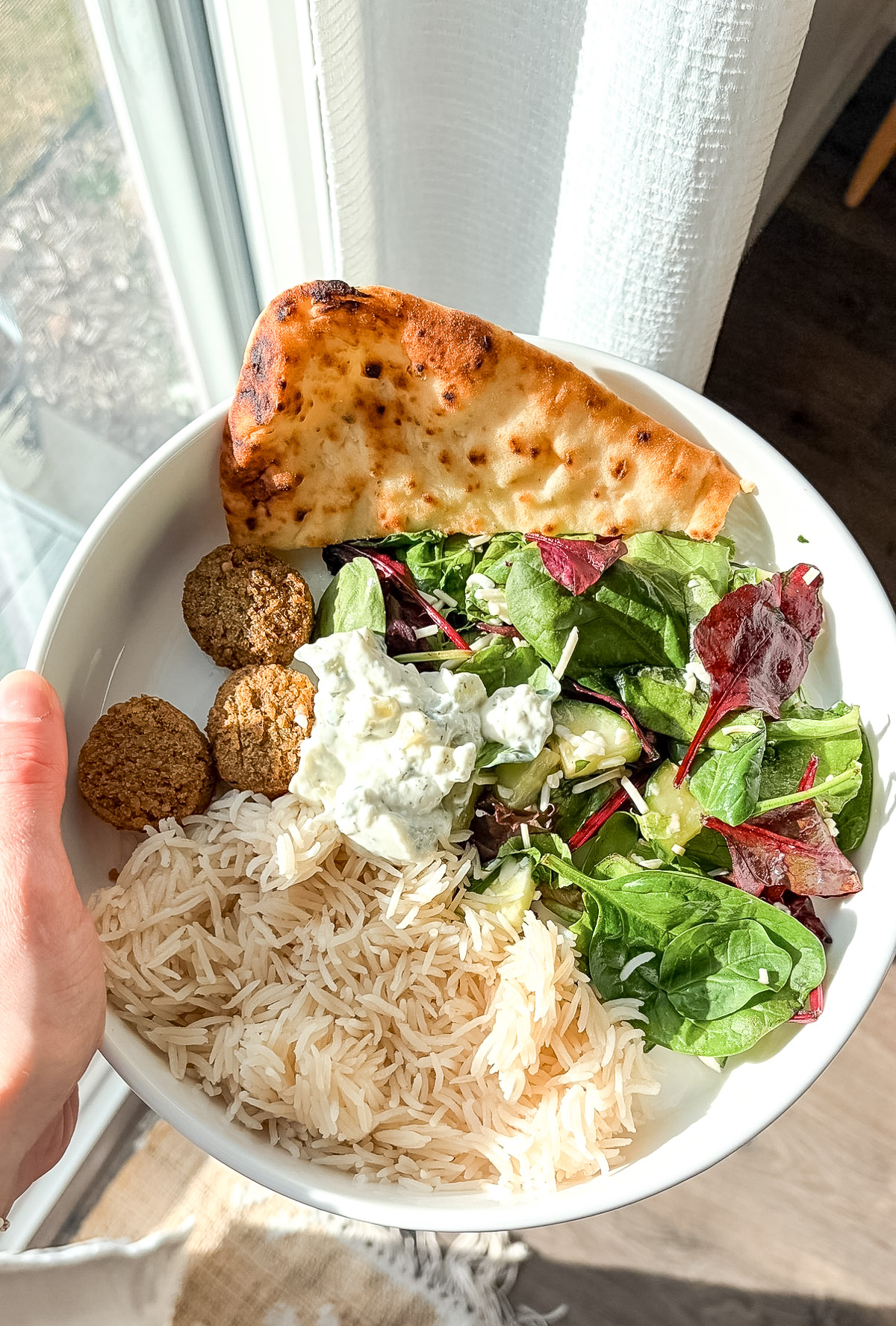 Falafel mediterranean bowl with rice, greens, naan bread, and tzatziki sauce.