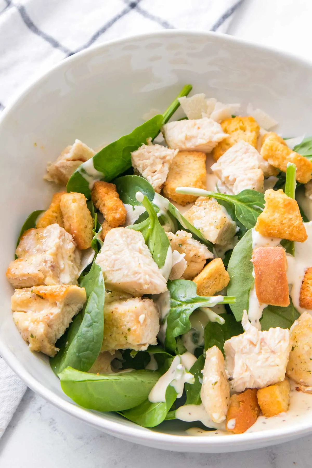 Spinach salad with air fryer chicken in a white bowl.
