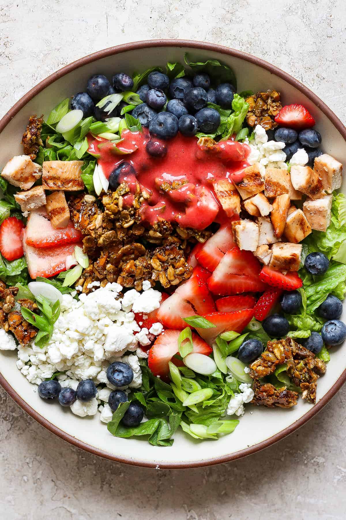 A green salad with chicken, berries, and crunchy granola in a large bowl.
