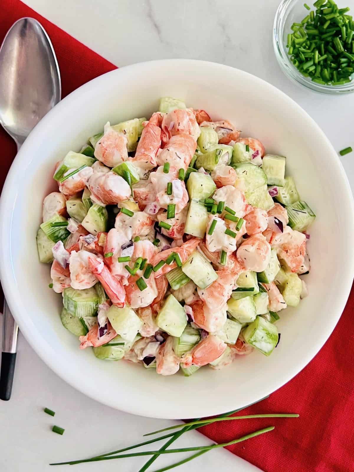 Creamy cucumber shrimp salad in a white bowl next to a spoon.