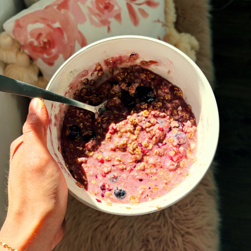 Woman holds white bowl of berry oatmeal with spoon in it.