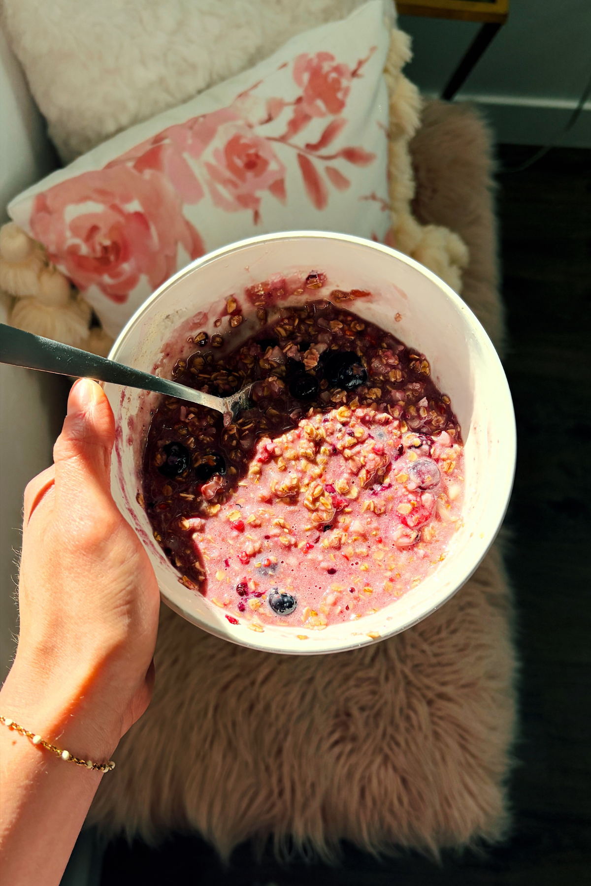 Woman holds white bowl of berry oatmeal with spoon in it.