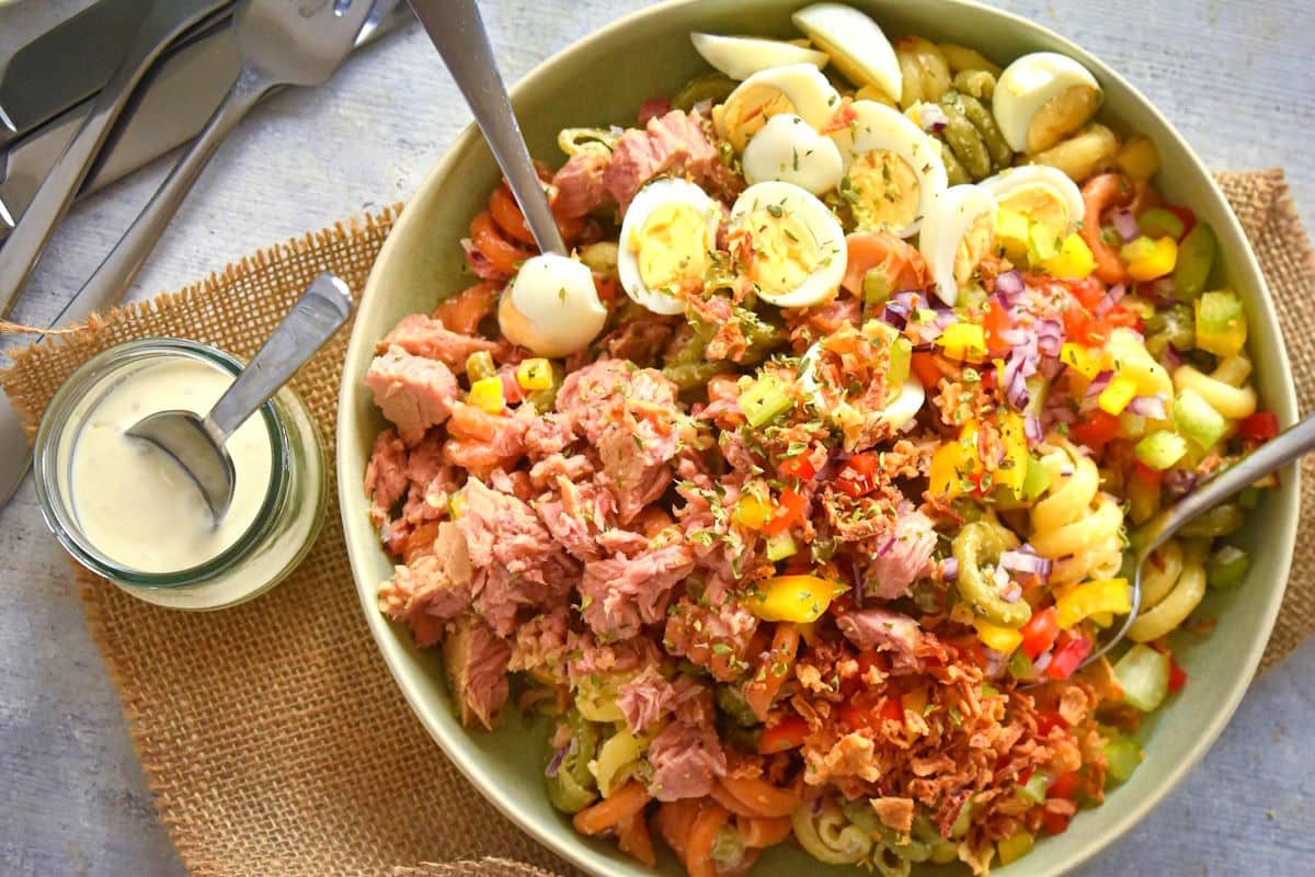 Creamy tuna pasta salad in a bowl with chopped eggs and veggies.