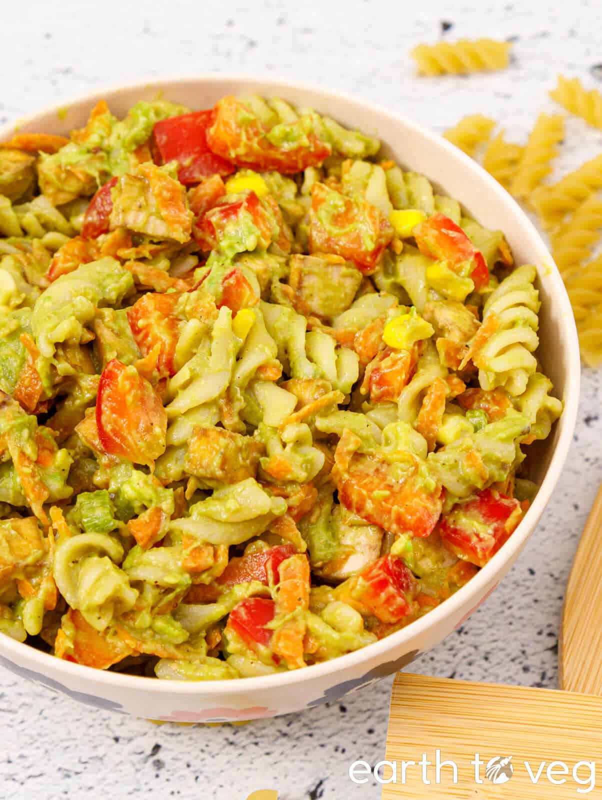 Creamy avocado pasta salad in a large white bowl with veggies.