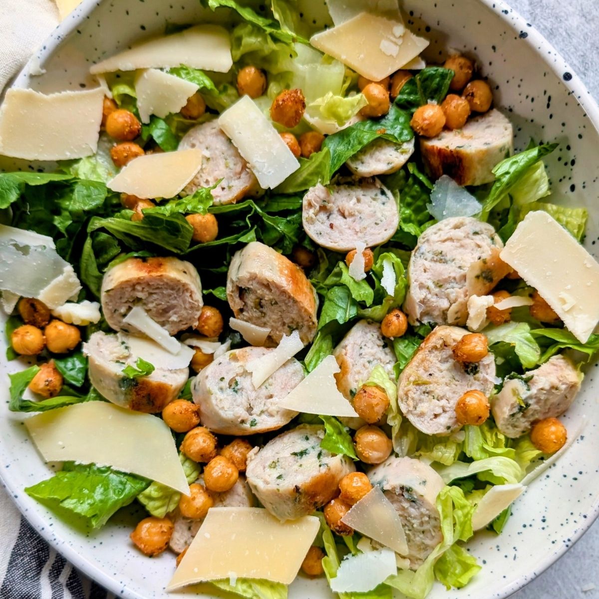 A Caesar salad with chicken sausage in a large white bowl.