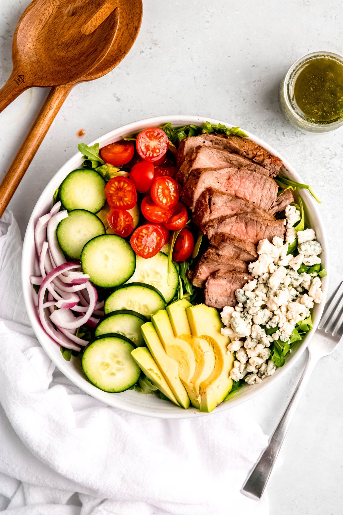 Grilled steak salad with veggies, avocado, and blue cheese in a white bowl.
